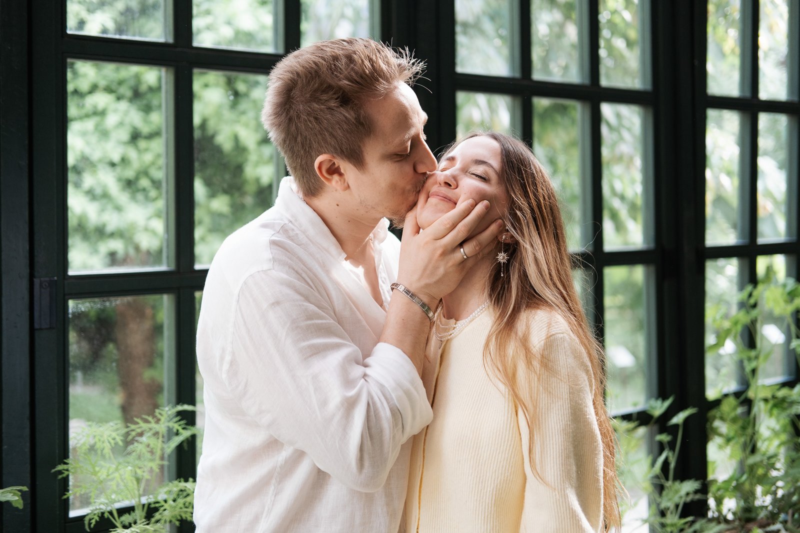 A man kisses a woman’s cheek, cupping her face tenderly as she smiles.