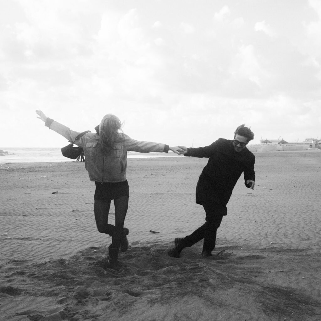 Coppia che corre mano nella mano sulla spiaggia durante un servizio fotografico prematrimoniale in Italia.