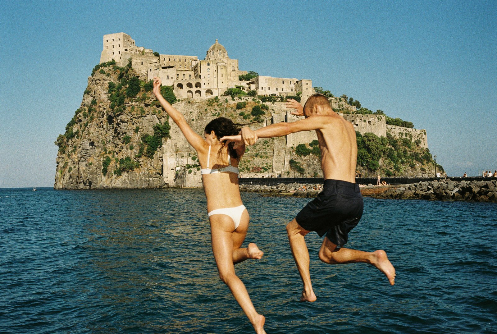 Couple jumping into the ocean near an Italian castle, shot on 35mm film.