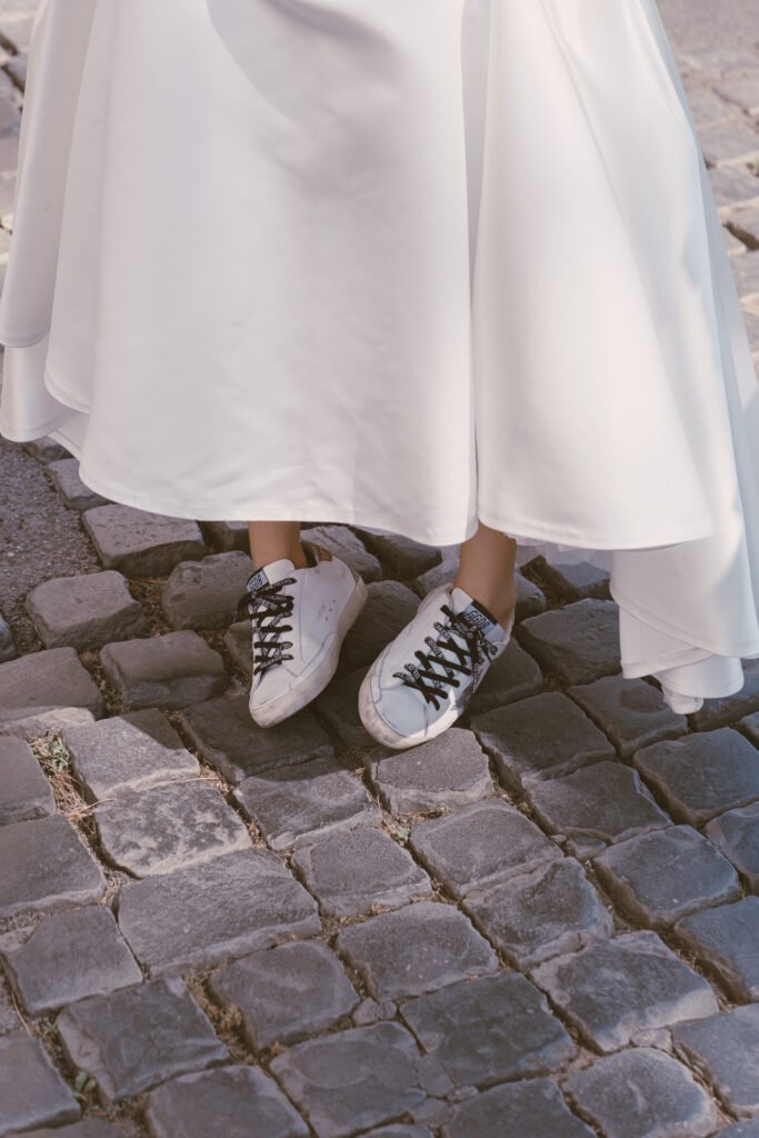 Close-up of a bride’s sneakers under her wedding dress on cobblestone street in Rome.