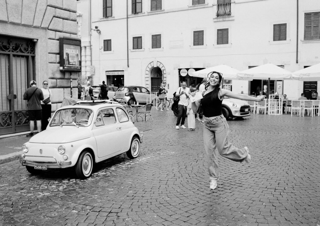 Woman jumping joyfully in front of a vintage Fiat 500.