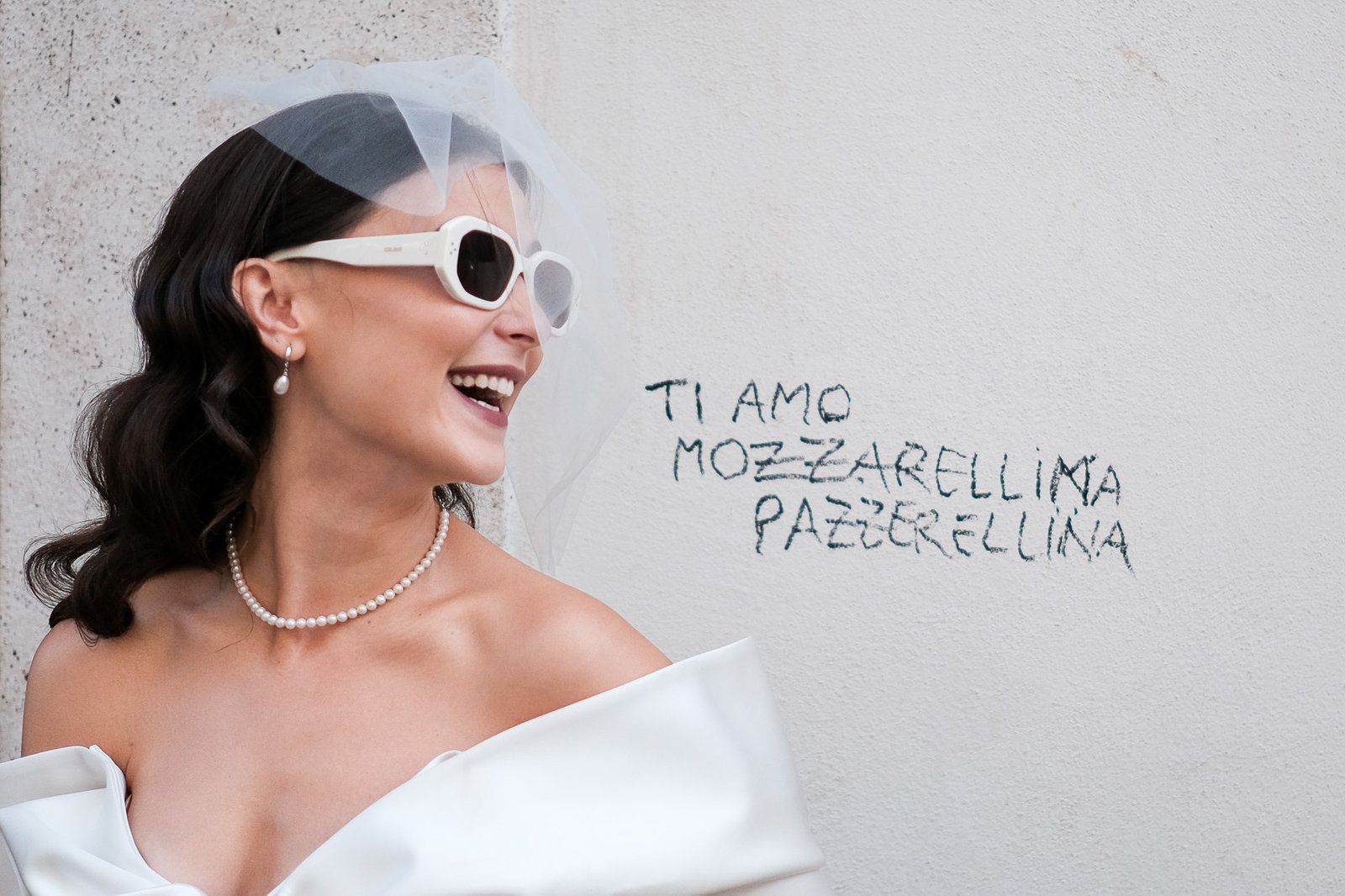 Stylish bride laughing with white sunglasses, modern wedding dress, and romantic writing on a wall in Rome, Italy wedding photography.