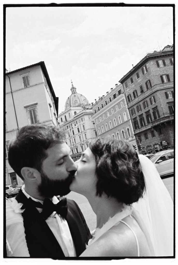 Bride and groom kissing in front of a Roman dome, captured on analogue film during their elopement.