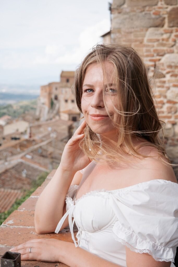 Donna in abito bianco sorridente davanti ai tetti di Montepulciano in Toscana.