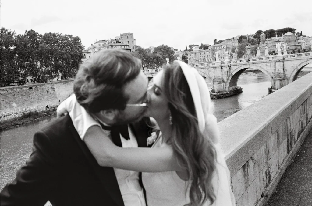 The Best Spots for Wedding Photography in Rome: A Guide to Capturing Your Love Story 1 Bride and groom kissing by the Tiber River during their Rome elopement wedding, captured on film.