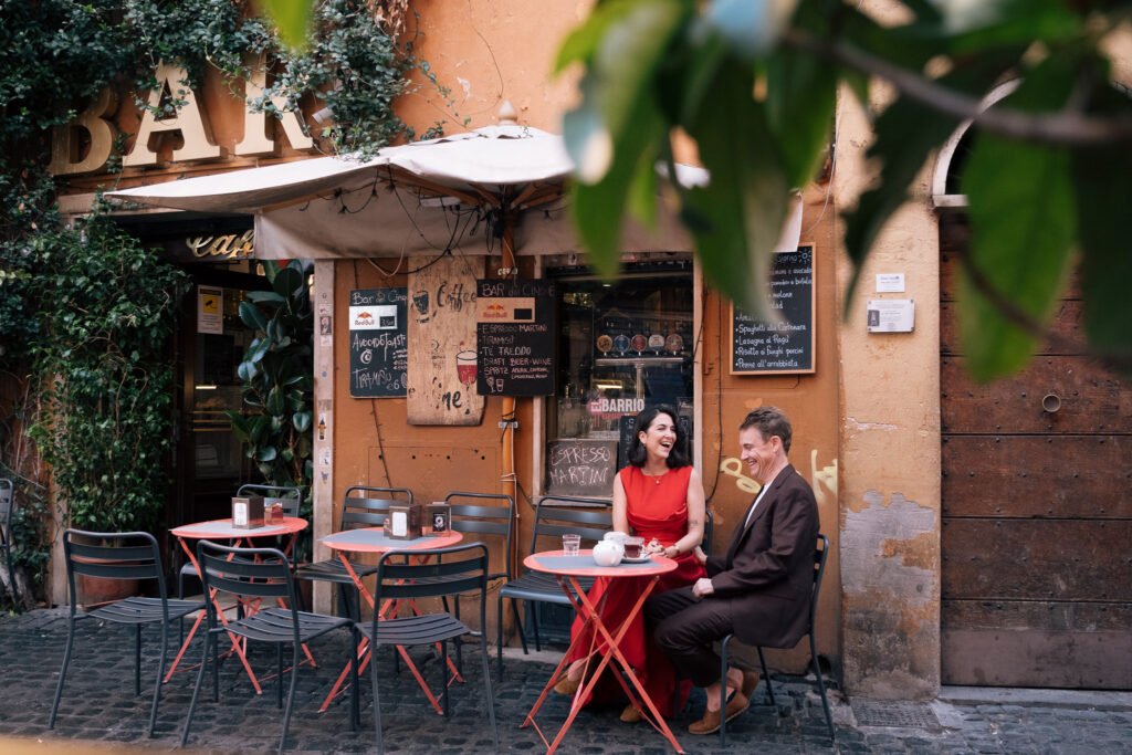 Couple laughing and drinking coffee at a café in Trastevere Rome during a vow renewal photoshoot.