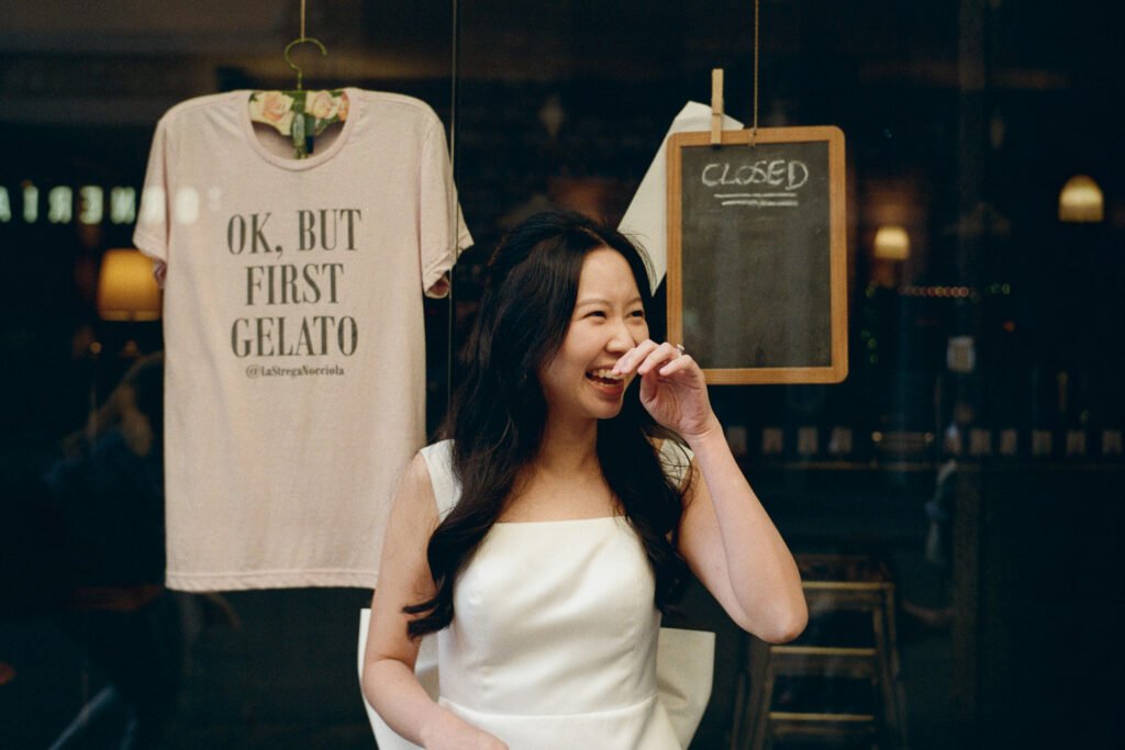 Donna che sorride davanti a una vetrina con la scritta “Ok, but first gelato” durante uno shooting su pellicola a Firenze.