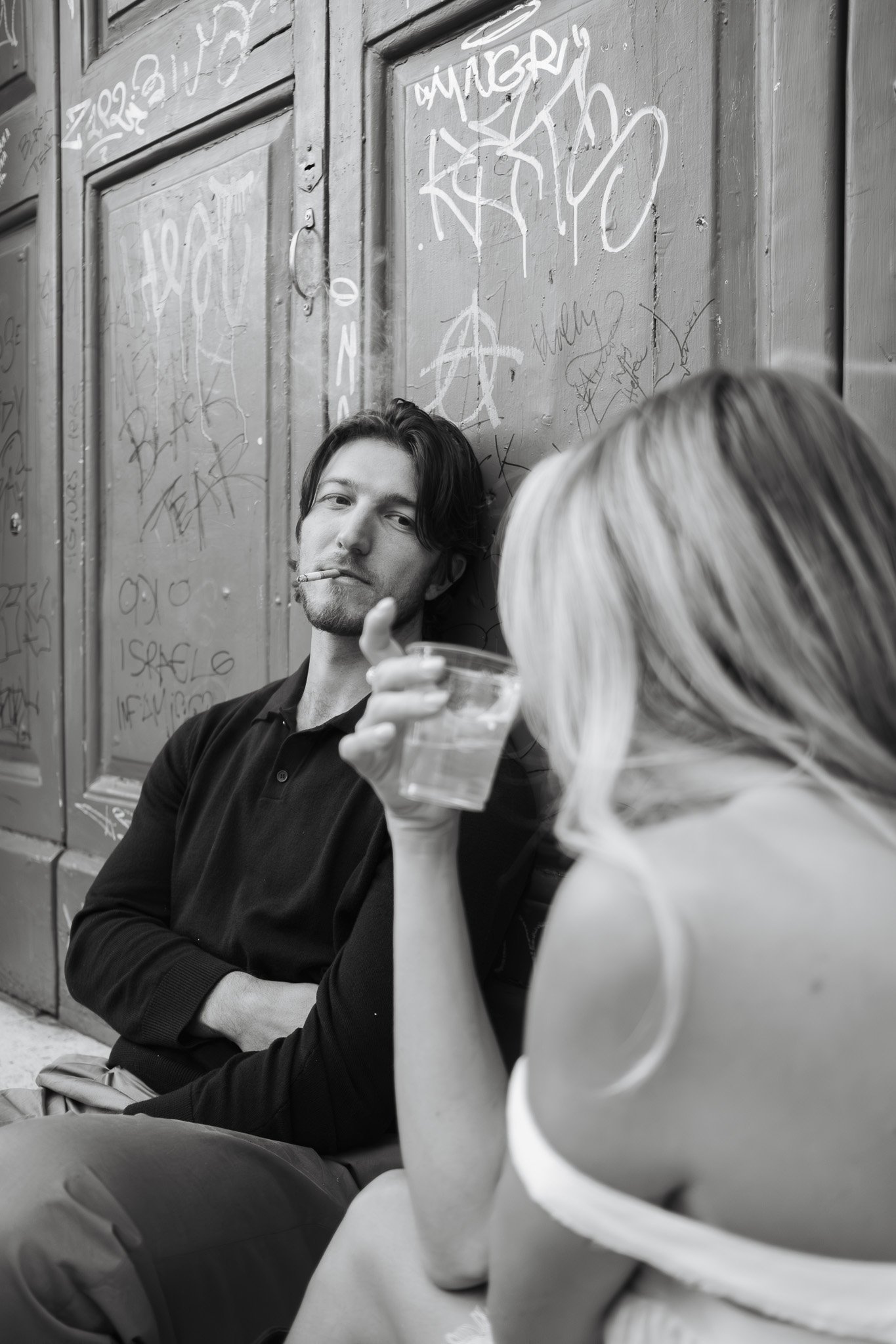 Couple sitting by graffiti wall with drink during engagement photoshoot in Rome by Gökhan Kutluer