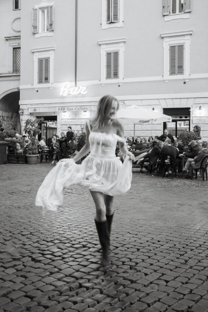 Woman in white lace dress dancing in front of Bar San Calisto during engagement photoshoot in Rome by Gökhan Kutluer