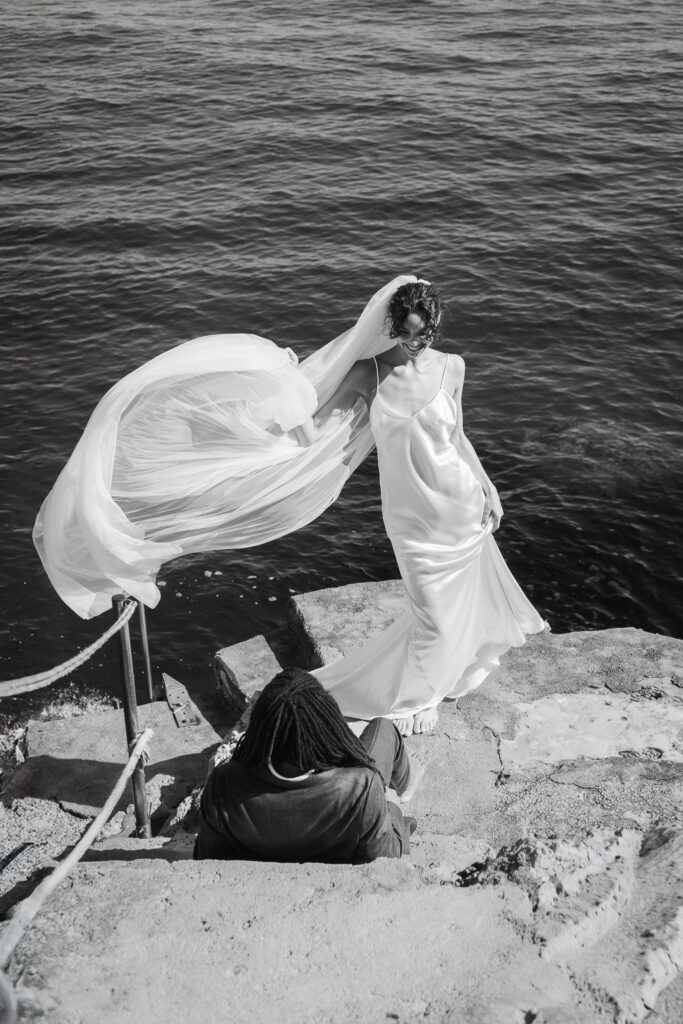 Bride with flowing veil standing on seaside steps in Sant’Elia Palermo Sicily