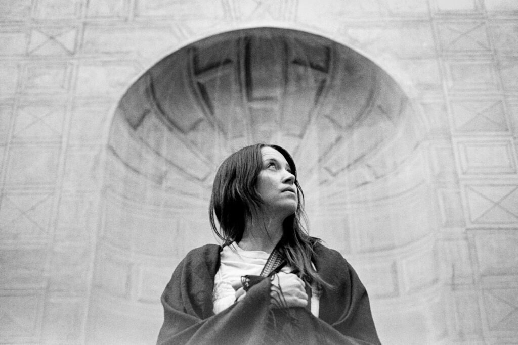 Black and white portrait of a woman standing beneath Roman architecture during a solo photoshoot in Rome, photographed by a personal photographer in Rome.