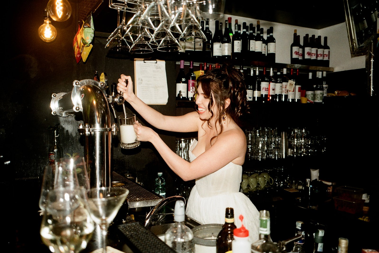 Bride pouring beer behind bar in Rome destination wedding reception, candid film wedding photography