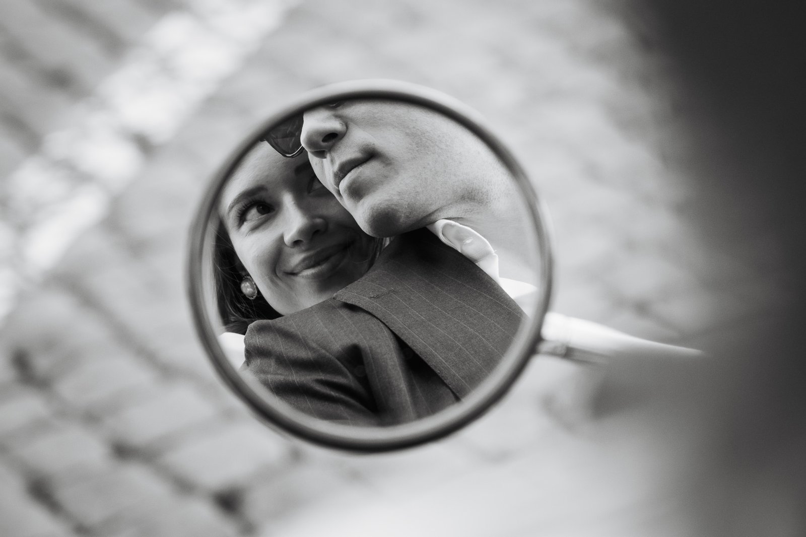 Riflesso in bianco e nero di una coppia durante il loro elopement a Roma: la sposa sorride felice mentre il viso dello sposo è appoggiato teneramente al suo, catturato in uno specchio rotondo. Foto intima di un fotografo elopement Roma.