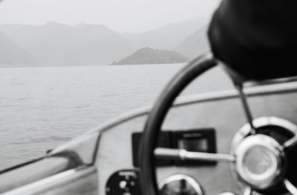 Close up detail of a luxury boat steering wheel with blurry mountains and water in the distance.