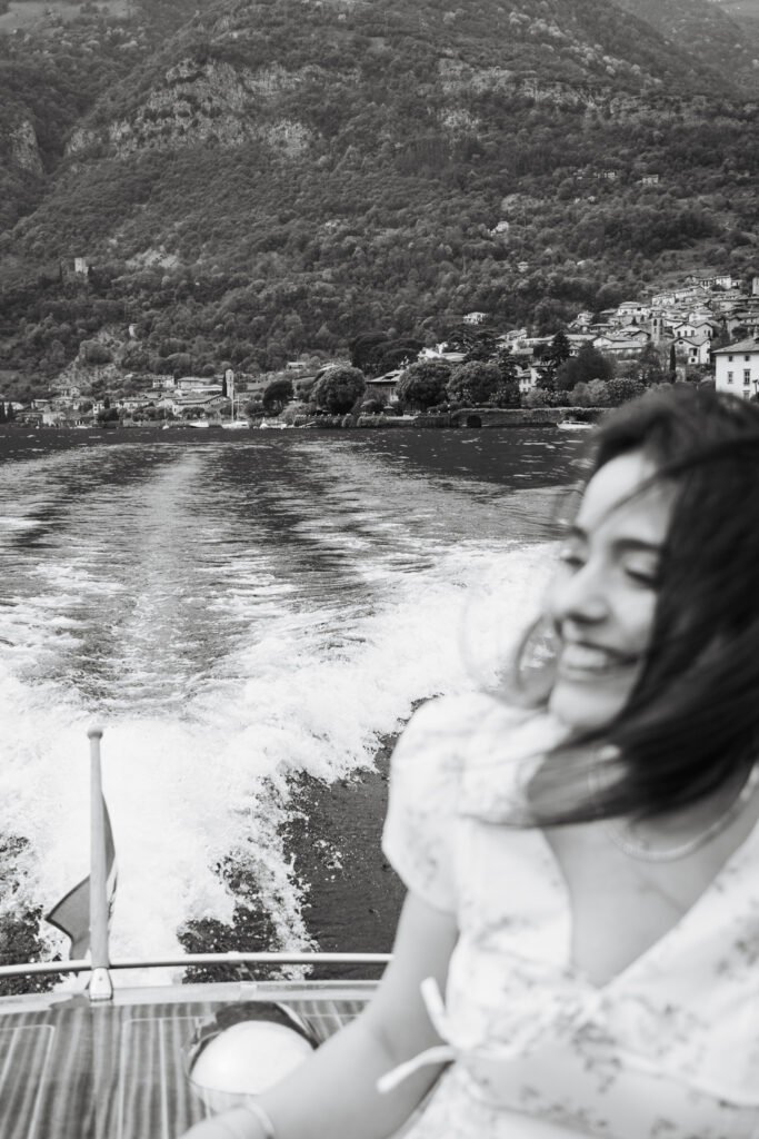 Moody black and white photography showing the wake of a boat and a woman smiling in the foreground.