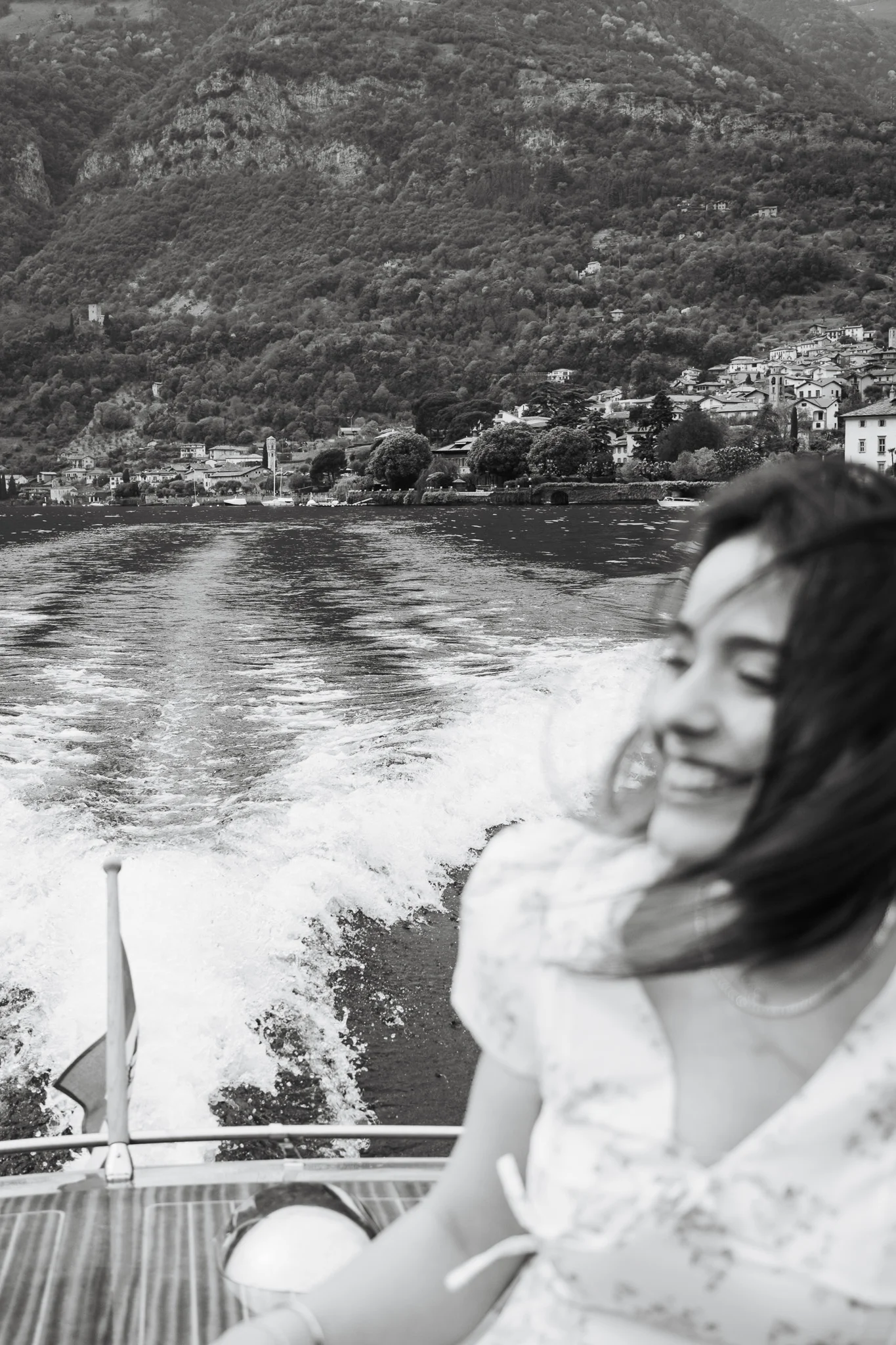 lake como proposal photographer ritrae momento spontaneo di una donna sorridente su una barca con montagne e borgo sullo sfondo