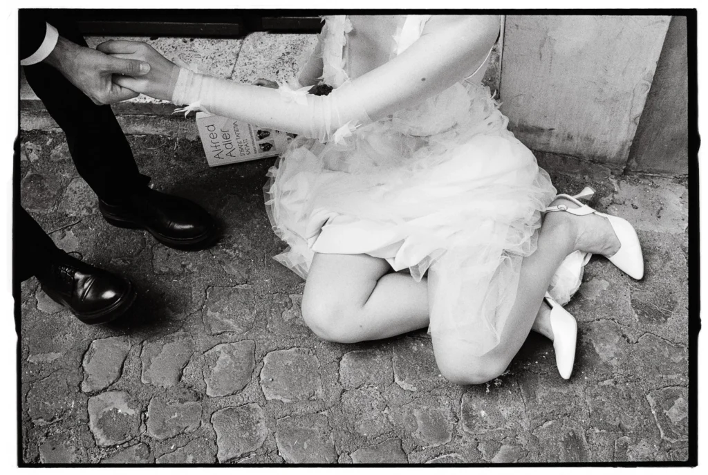 Black and white photograph of a bride and groom holding hands while sitting on ancient Roman cobblestones during their intimate elopement in Rome. Captured by a local Rome elopement photographer.