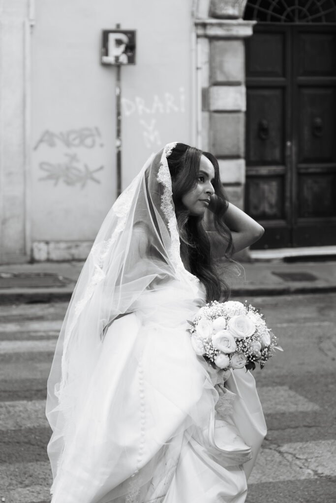 Bride Ariam walking through Rome street in veil holding bouquet black and white cinematic wedding photography Rome