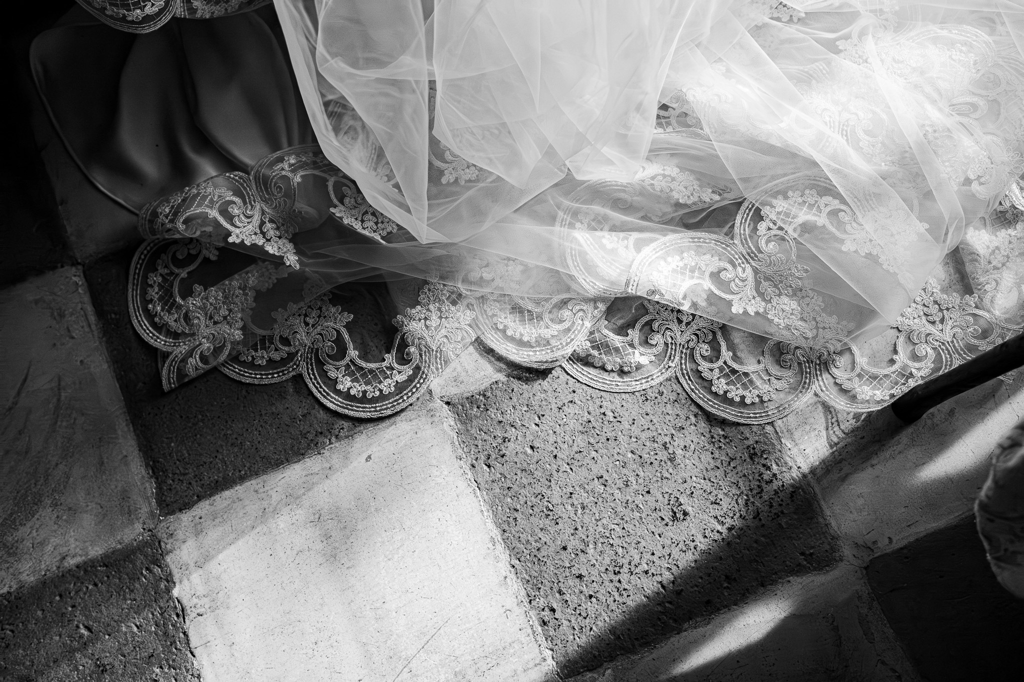Un primo piano fotografico in bianco e nero del velo da sposa in pizzo adagiato su un pavimento in pietra antico in Italia, catturato da un documentary wedding photographer.