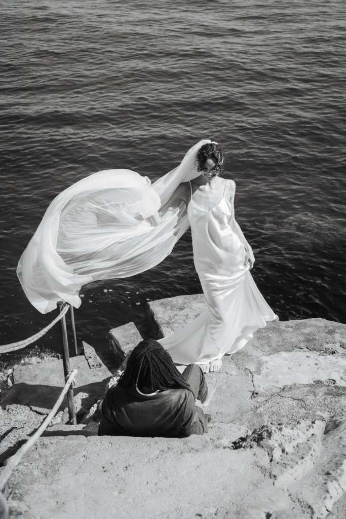 Bride laughing by the sea with her veil blowing in the wind during a documentary wedding photoshoot in Italy.