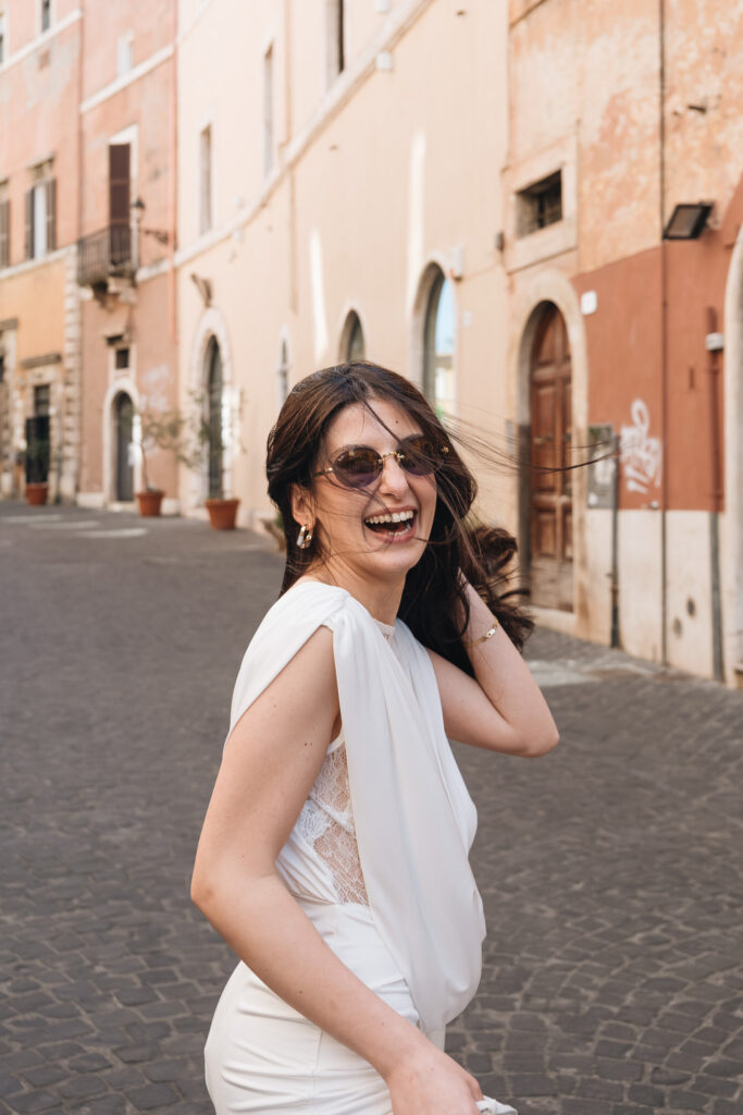 Easygoing bride Cemre laughing in sunglasses on the streets of Tivoli during her wedding photoshoot near Rome.