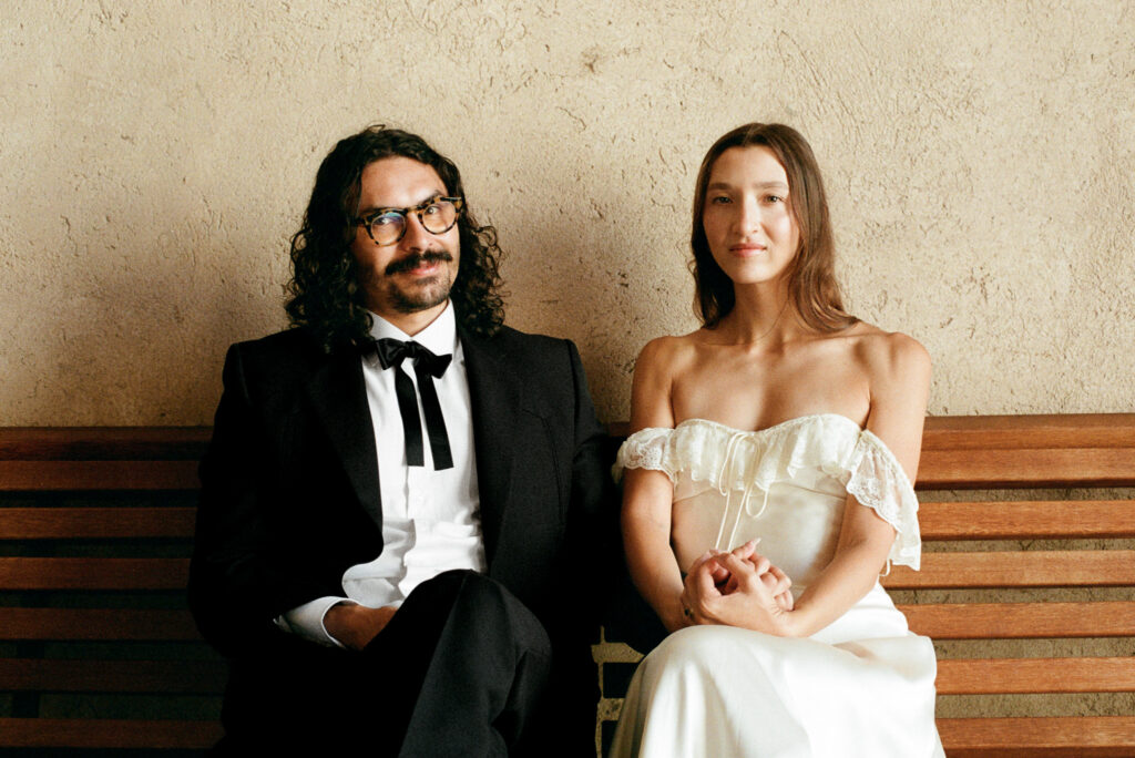 Bride and groom sitting together on a wooden bench during their intimate elopement in Spello, Umbria, photographed on color film.