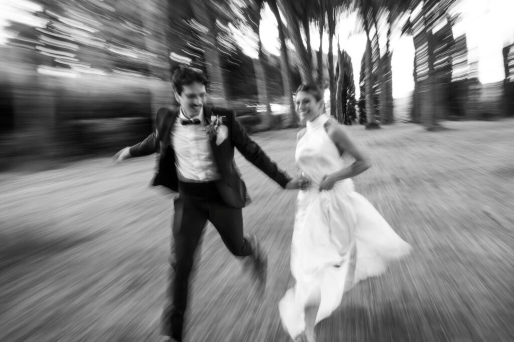 Foto di matrimonio in bianco e nero di Hande e Matteo che corrono mano nella mano nel giardino di Relais Villa Lina a Roma, con effetto mosso creativo, realizzata da un fotografo di matrimonio a Roma.