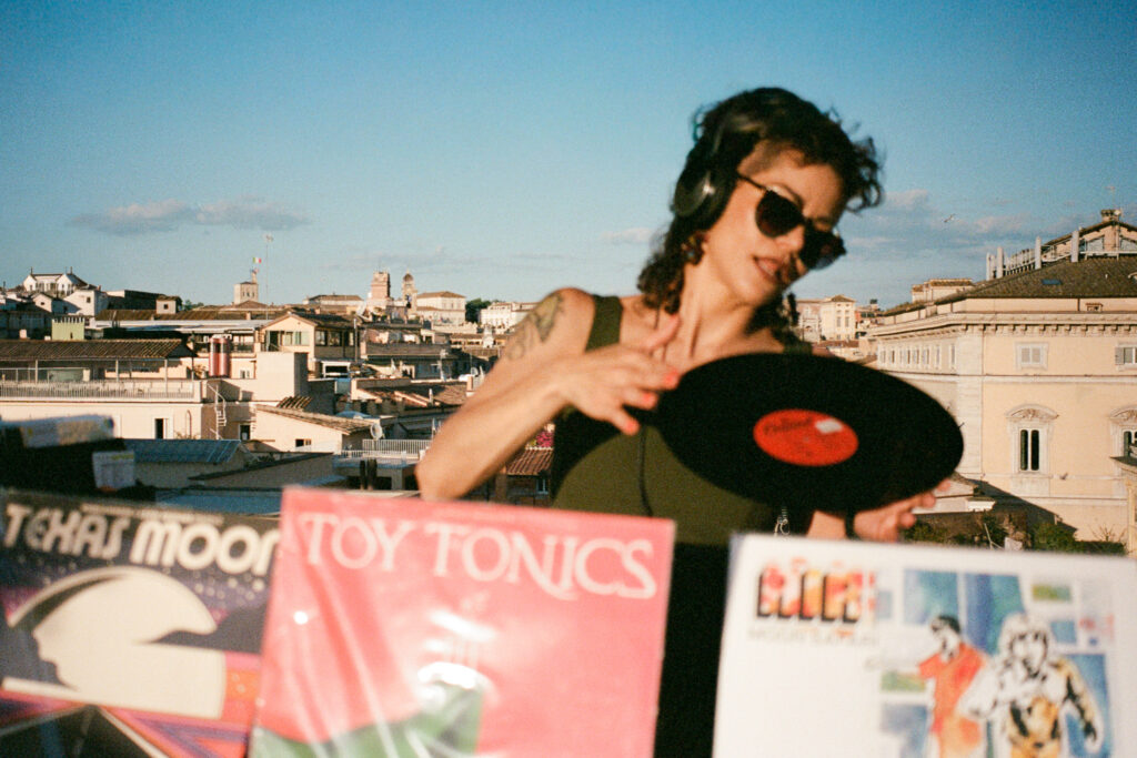 The wedding DJ holds a vinyl record above a table of albums overlooking the rooftops of Rome.