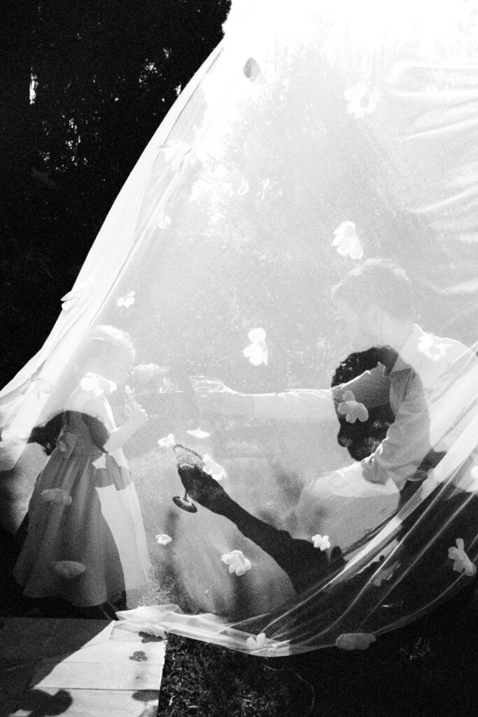 Bride groom and child playing under a floral veil during a film wedding in Cefalù Sicily