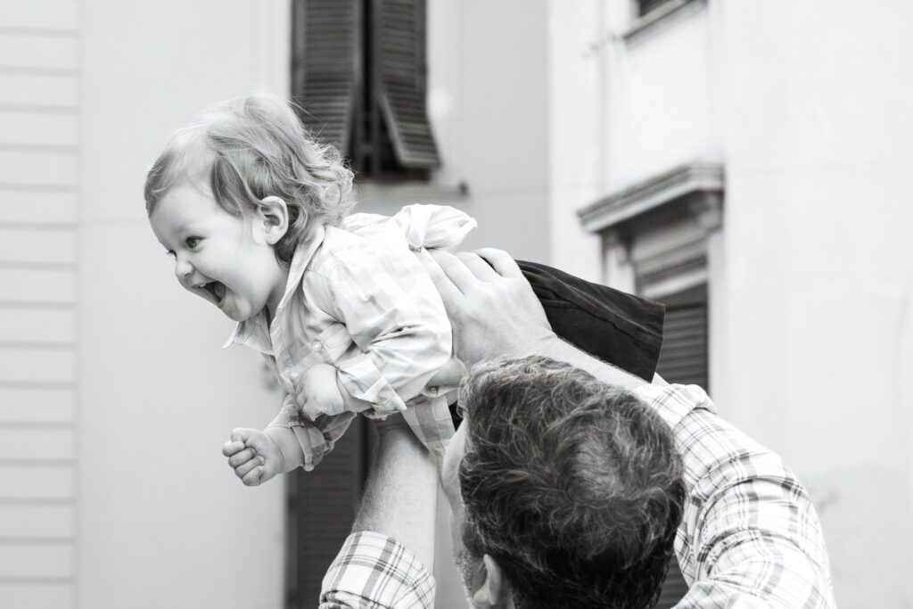 Father lifting his laughing toddler into the air during a candid family photoshoot in Rome, Italy.