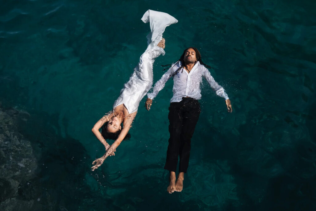 Bride and groom floating hand in hand in the Mediterranean after their destination wedding in Sicily.
