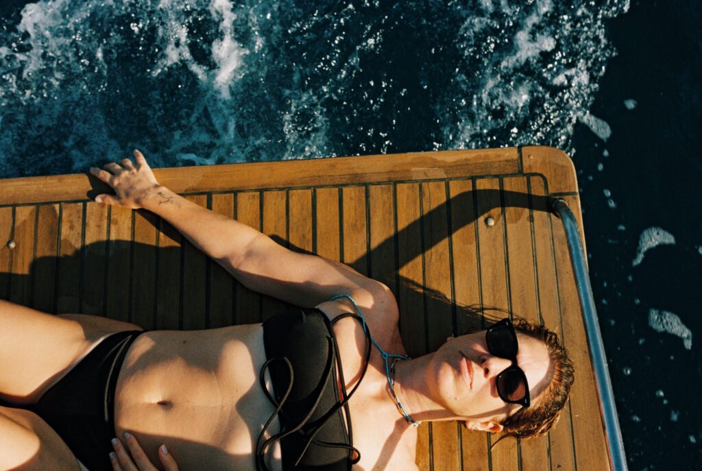 Woman in a black swimsuit and sunglasses relaxing on a boat during a 35mm film portrait session in Italy
