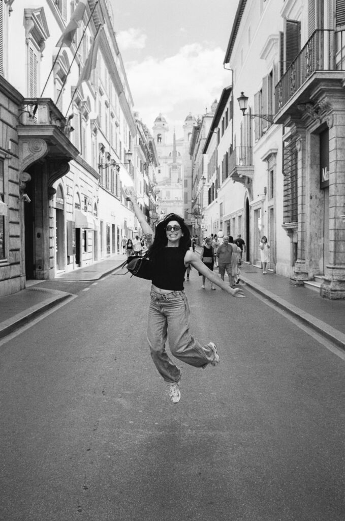 Woman jumping playfully on Via Condotti in Rome with the Spanish Steps in the background