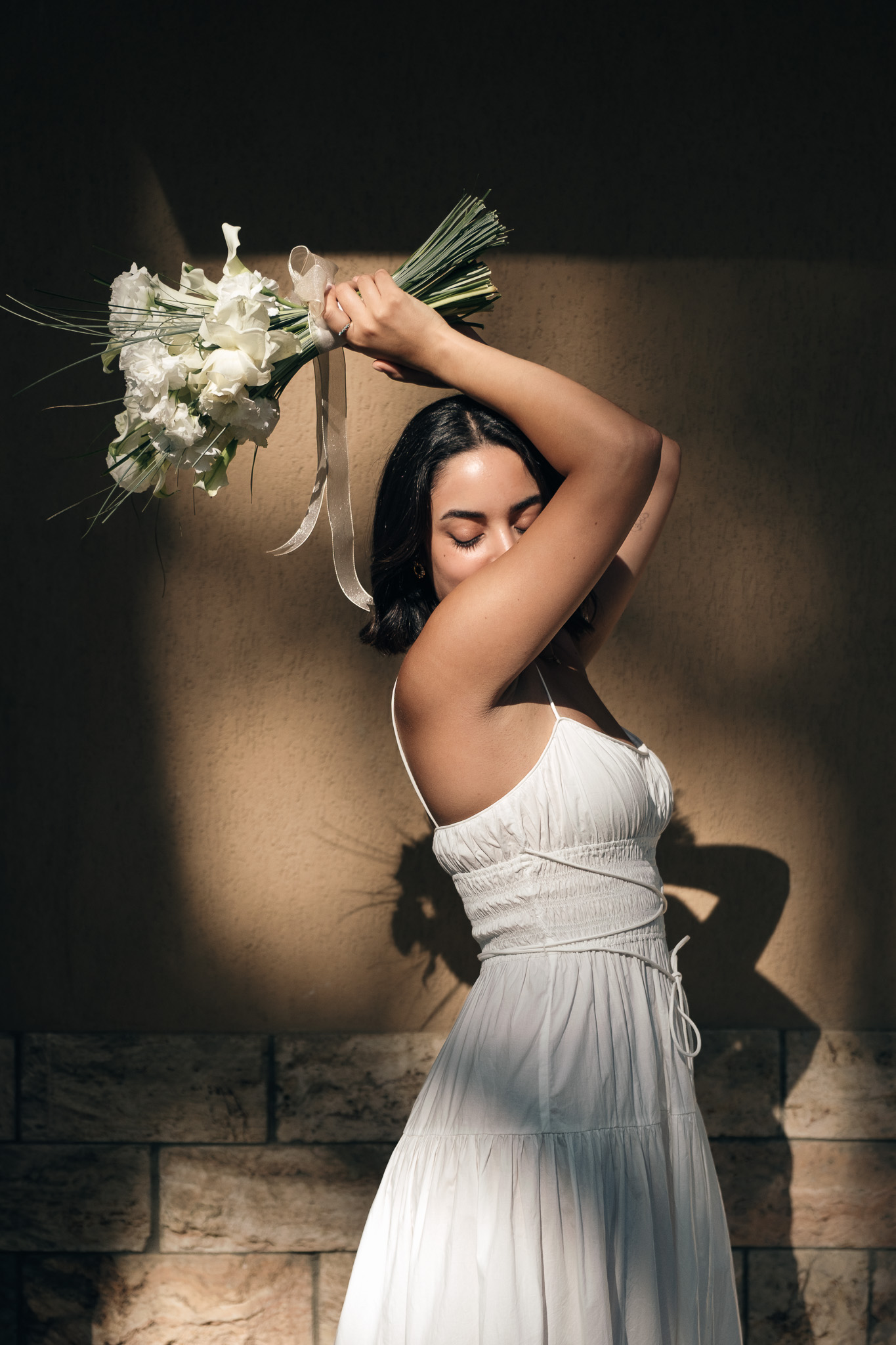 Bride holding her bouquet above her head in dramatic sunlight during a full day Tuscany elopement in Val d’Orcia.