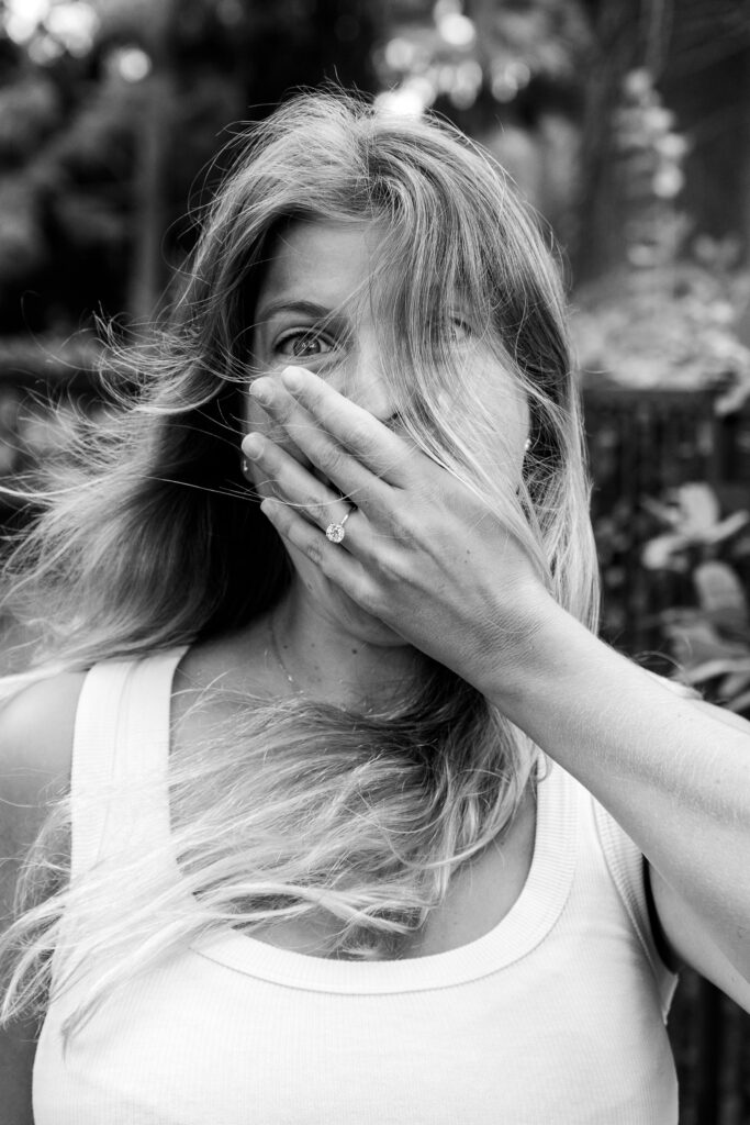 Black and white close-up of a woman reacting with surprise after a proposal in Villa Borghese, Rome, with her engagement ring visible on her hand.