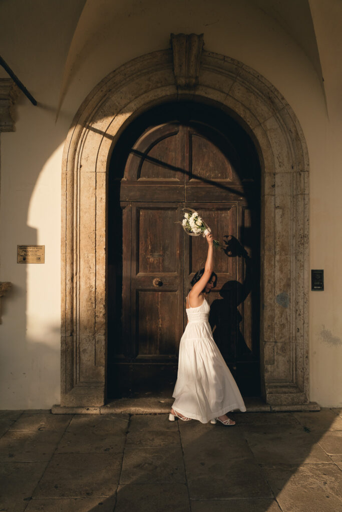 Sposa in abito bianco davanti alla chiesa di San Biagio a Montepulciano, illuminata dal sole del pomeriggio.