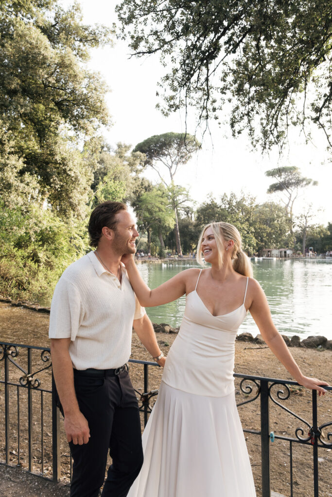 Honeymoon couple smiling beside the lake in Villa Borghese during a relaxed Rome honeymoon photoshoot.