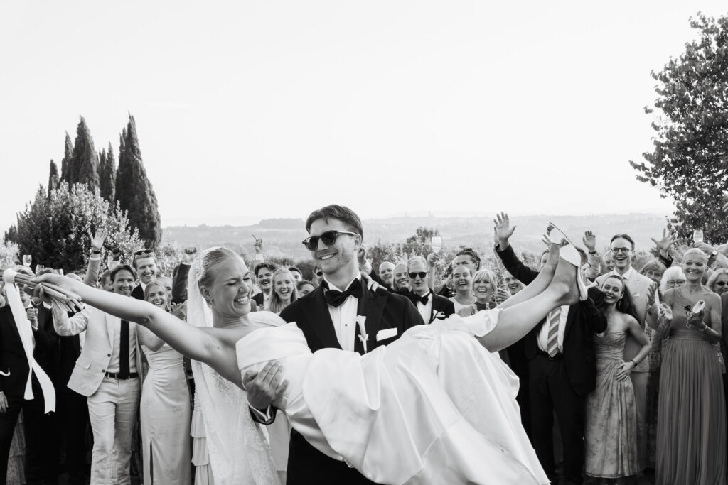 Bendik tiene Mathilde tra le braccia mentre gli invitati festeggiano intorno a loro durante il matrimonio a Villa Catignano.