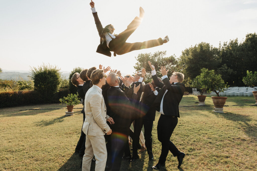Bendik viene lanciato in aria dagli amici nel giardino di Villa Catignano durante il matrimonio al tramonto in Toscana.