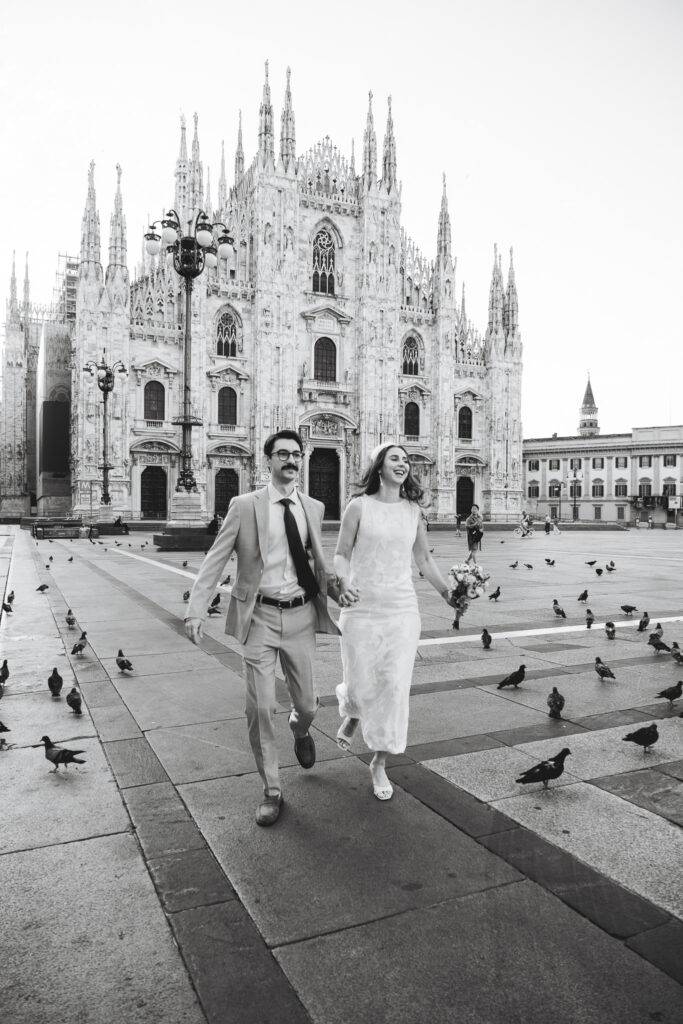 Bride and groom walking hand in hand across Piazza del Duomo with Milan Cathedral behind them