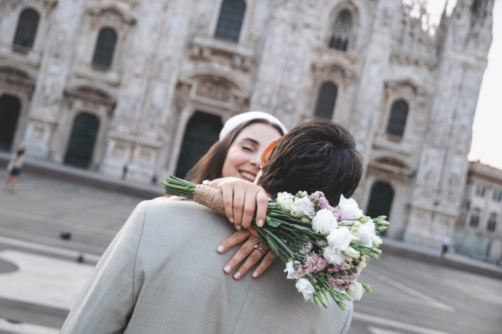 Bride embracing groom with wedding bouquet in front of Milan Duomo