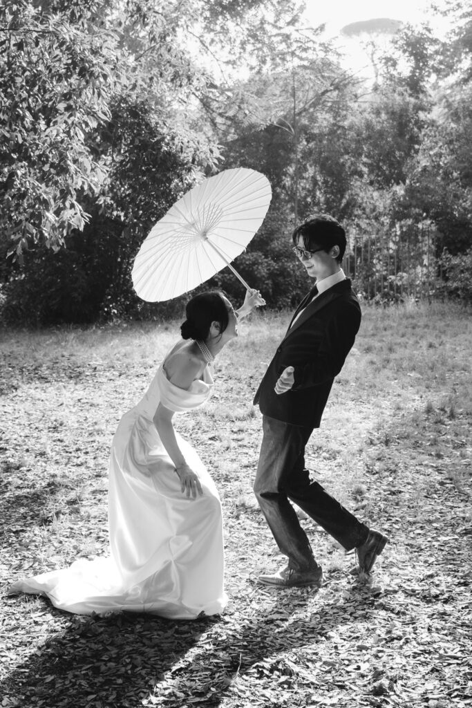 Playful Japanese couple Kanaka and Sakitu laughing with a white parasol in the gardens of Villa Borghese during their Rome pre wedding photoshoot.
