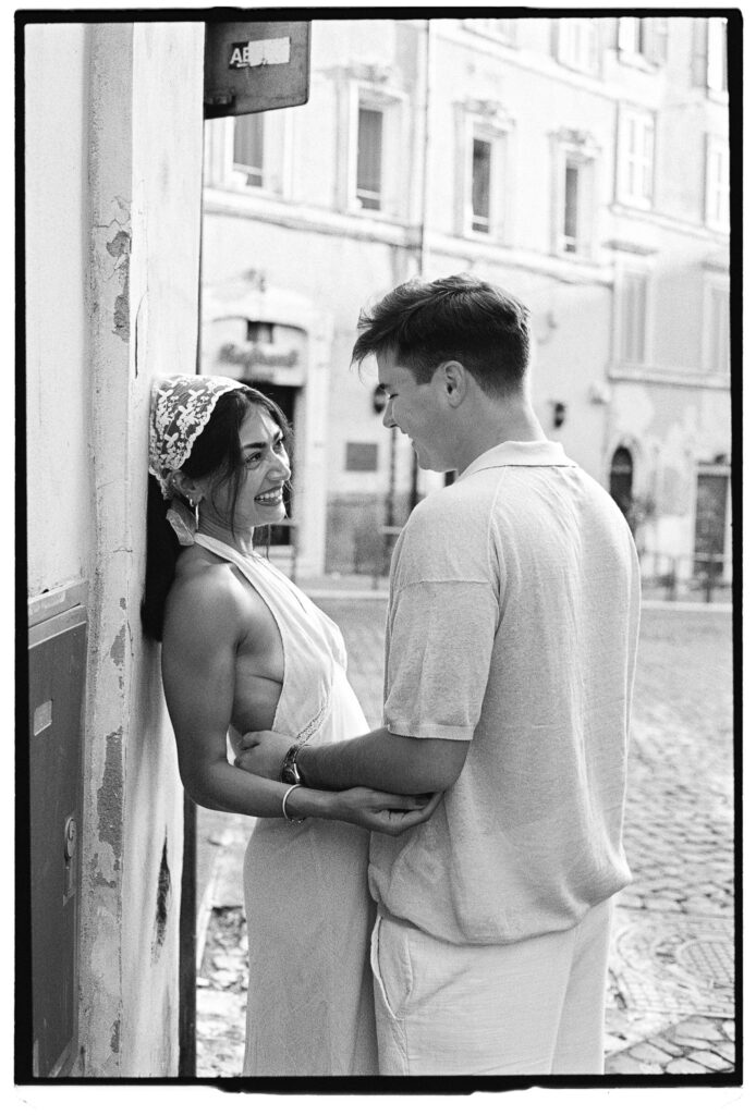 Aditi e il suo compagno sorridono insieme durante un servizio fotografico di coppia a Roma su pellicola in bianco e nero.