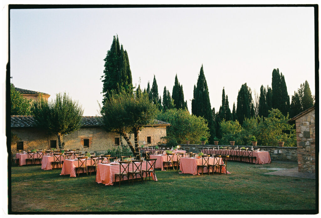 Outdoor wedding dinner tables with red gingham tablecloths surrounded by cypress trees at Villa Catignano in Tuscany.