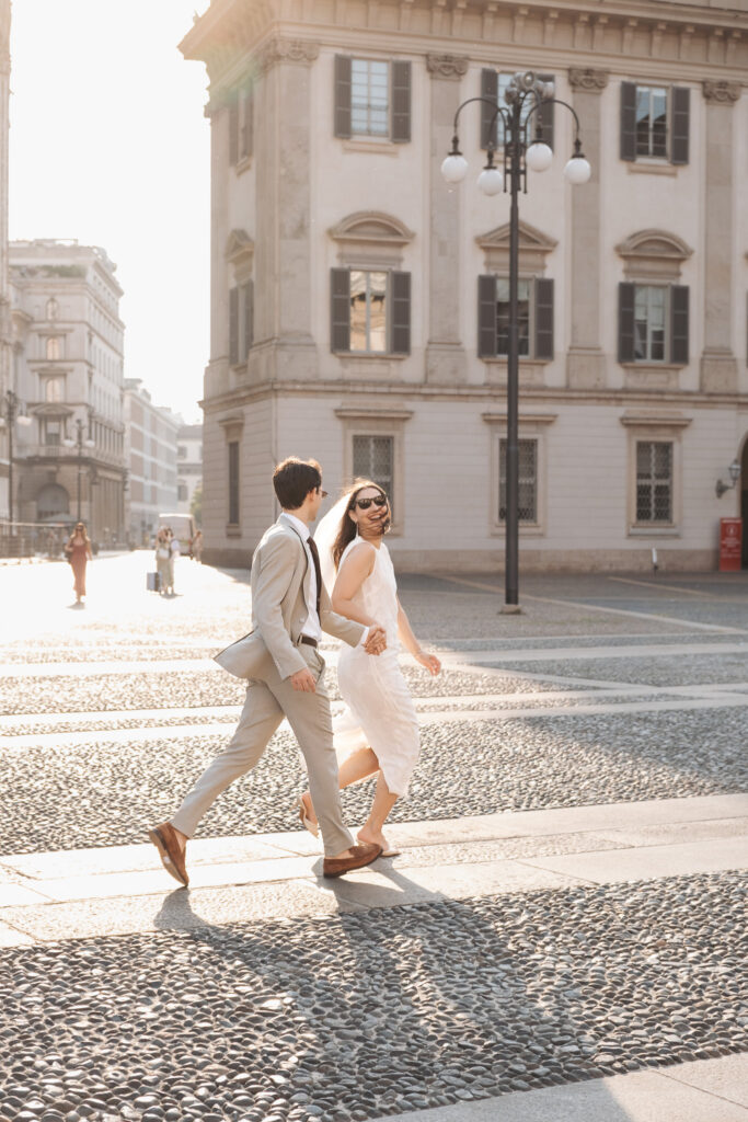 Newly married couple walking hand in hand through central Milan in wedding outfits