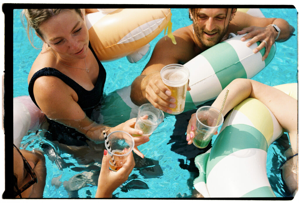 Wedding guests raising drinks together in a swimming pool during a Sicily wedding weekend on 35mm film.
