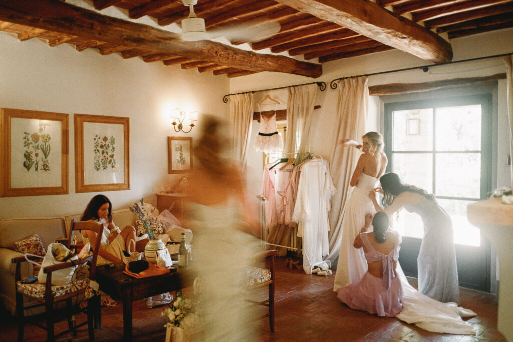 Bride getting ready with friends helping her dress in a rustic room, photographed in warm natural light on 35mm film.